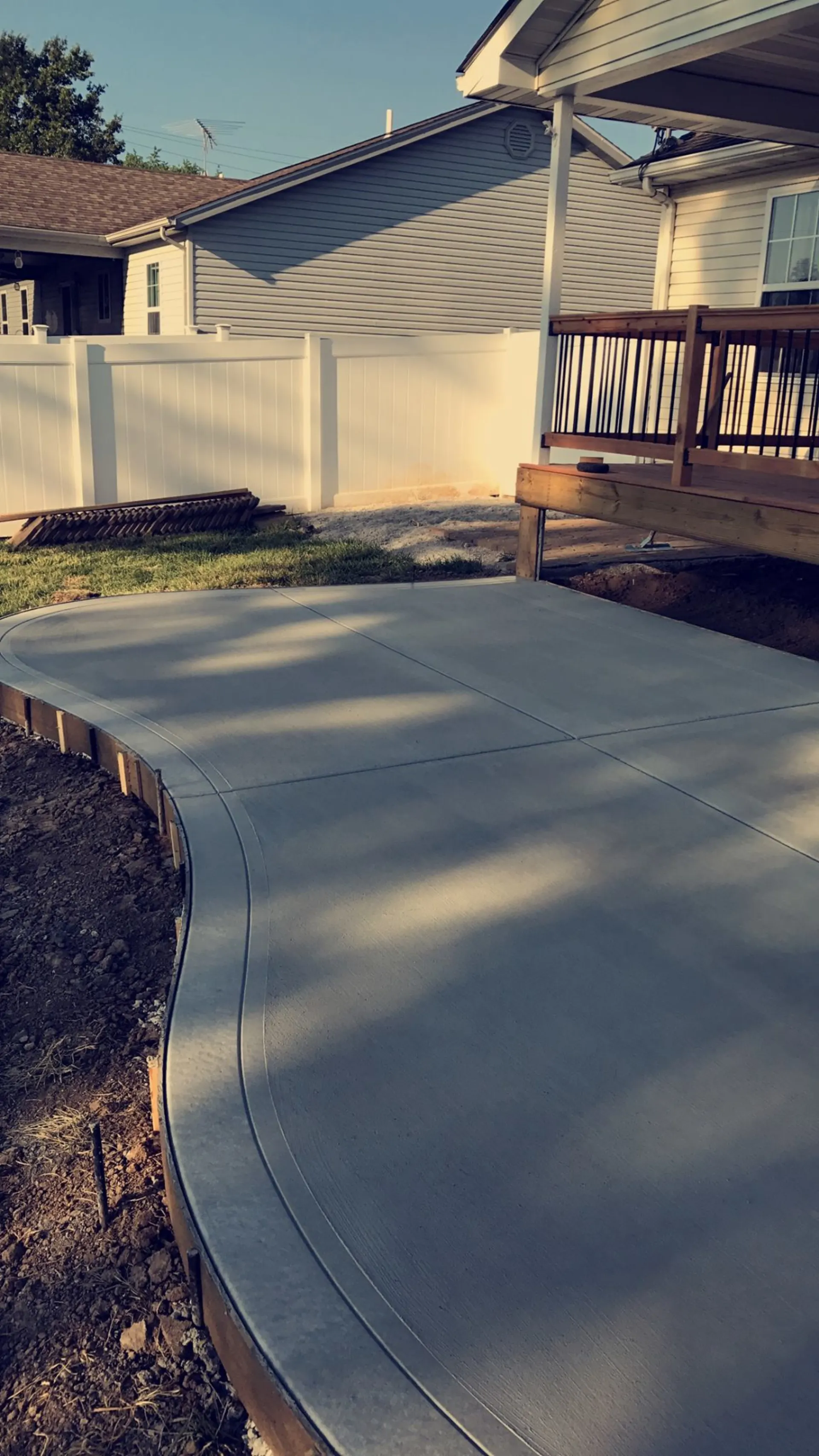Curved smooth concrete patio next to a wood deck in a residential backyard
