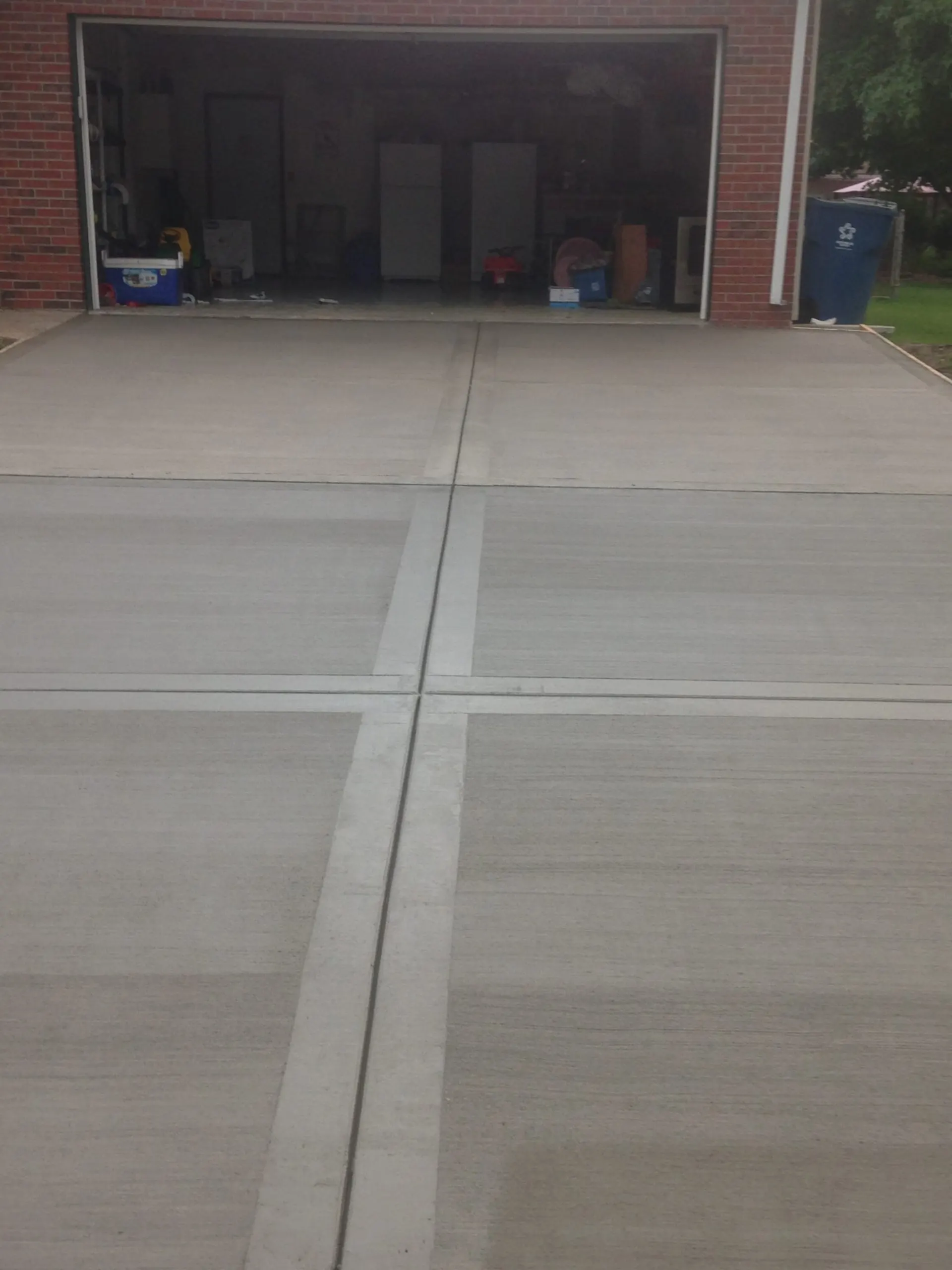 Smooth concrete driveway with saw-cut control joints in front of a brick garage