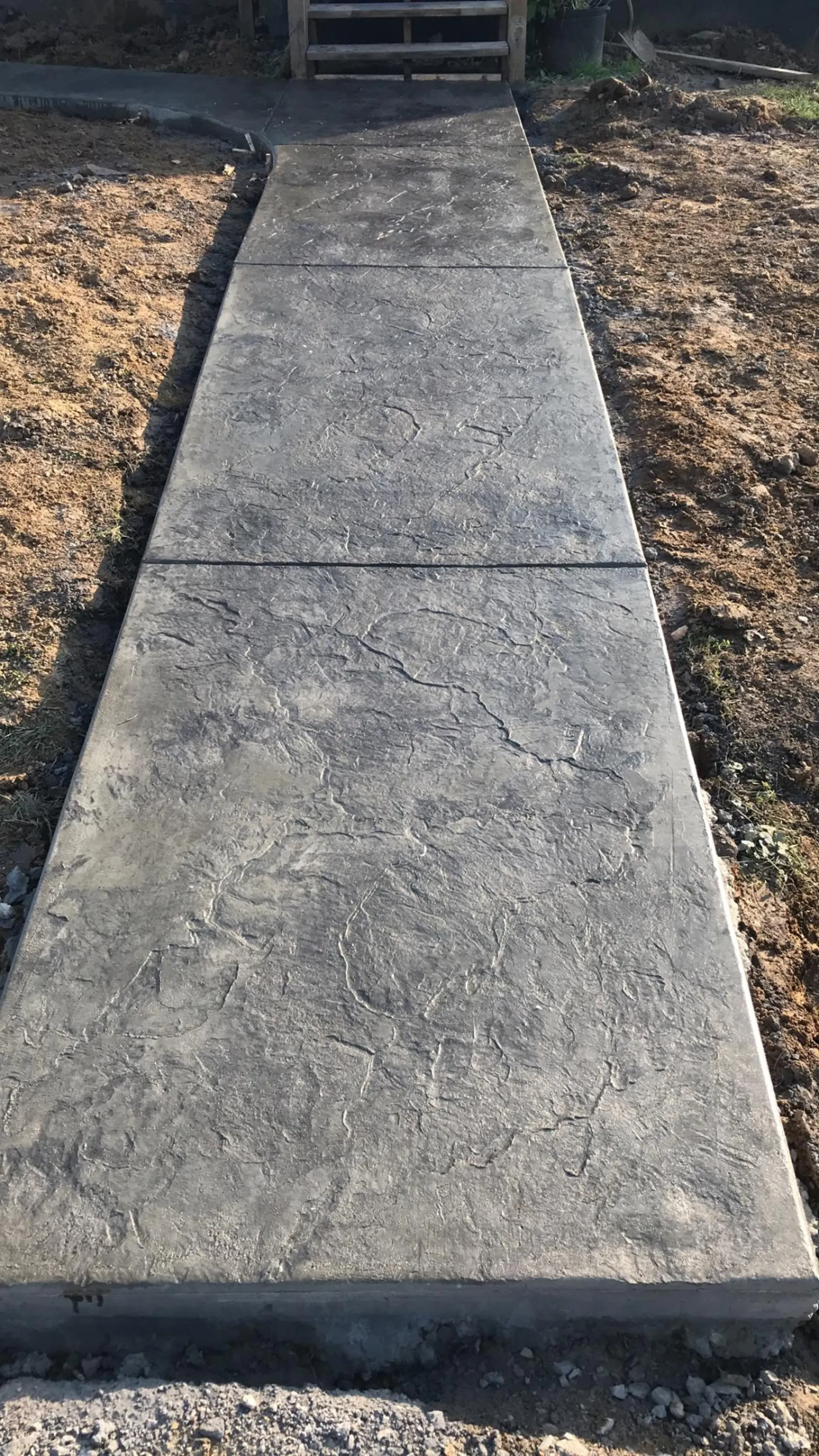 Sunlit stamped concrete walkway with deep slate texture